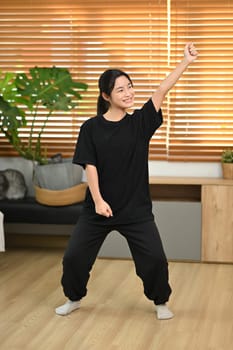 Cheerful young asian woman having fun, practicing a dance move in a living room.