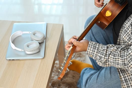 Young man sitting on sofa and playing an acoustic guitar. Leisure, hobby and activity concept.