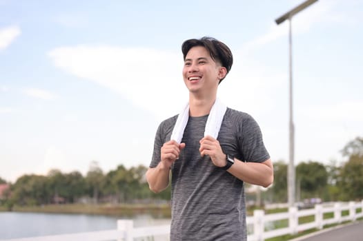 Smiling young asian man jogging in the park on cloudy day. Fitness and active lifestyle.