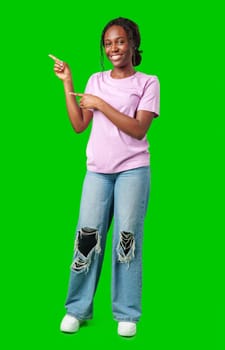 A young girl stands confidently pointing to the right against a bright green backdrop in studio