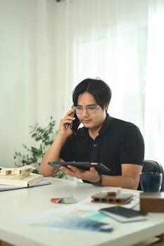 Professional architect discussing project plans over phone and using digital tablet in the office.