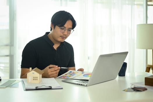 Professional interior designer working with color swatches and planning home design project online on his laptop.