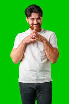 A man with a beard smiles mischievously while clasping his hands together against a bright green background close up