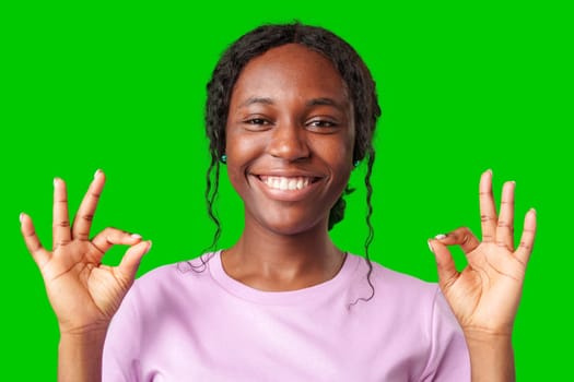 Young woman smiling and making a positive gesture against a bright green background in studio