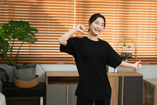 Cheerful young asian woman having fun, practicing a dance move in a living room.
