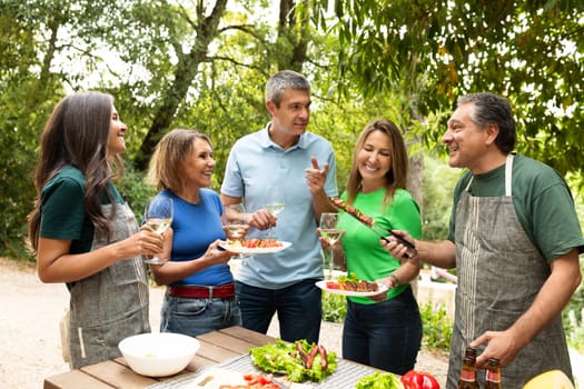 Friends celebrate together at a barbecue, sharing laughter and delicious food in a verdant garden. The sun shines as they toast with drinks and savor the moment.