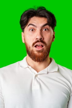 Surprised young man with a beard expressing shock against a bright green background in a casual setting