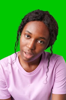 Young woman with curly hair shows a skeptical expression against a bright green background in studio