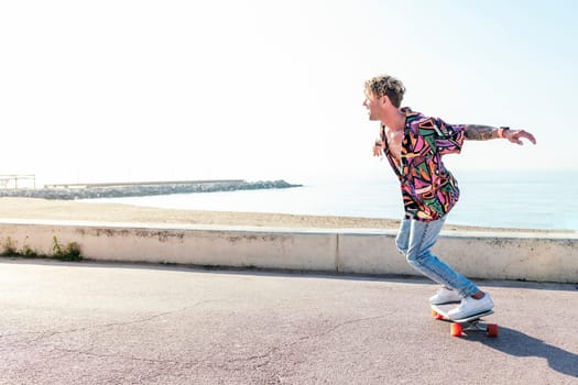 stylish male hipster in trendy wear riding modern skateboard with outstretched arms while balancing and enjoying weekend in summer