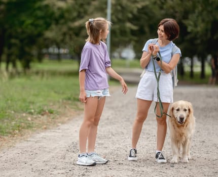 Girl And Mother Walking With Golden Retriever Dog At The Park And Having Fun