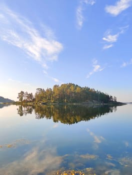 Baltic sea on a completely calm summer day. Small island on Finnish archipelago with reflection in water on the horizon