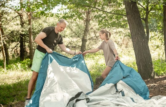 Father And Daughter Setting Up A Tent While Camping In The Forest
