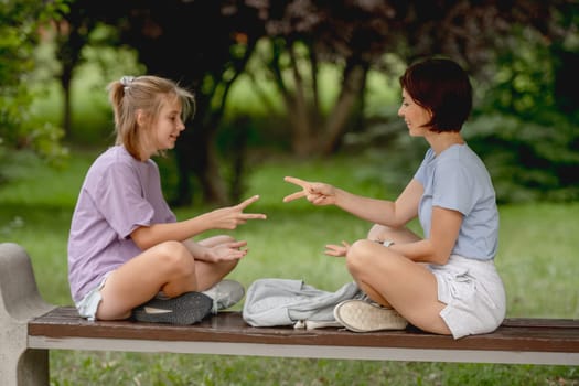 Mother And Daughter Happily Playing Rock, Paper, Scissors Outdoors