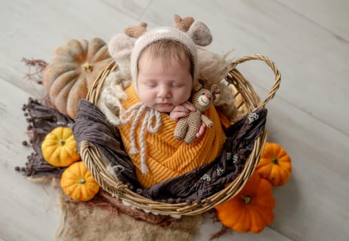Newborn baby girl swaddled in white fabric sleeping in basket decorated with pumpkins. Infant child kid napping on fur autumn studio portrait