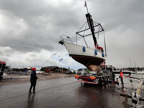 Espoo, Finland, September 22, 2024 - Sailboat lifted by a crane from the water for winterization in winter, Finland, Baltic Sea, Gulf of Finland