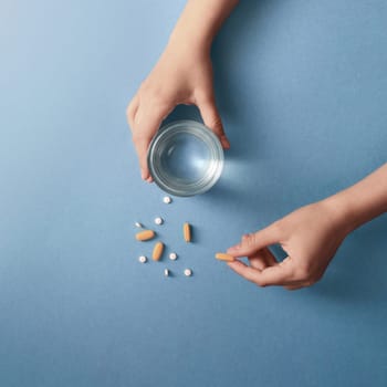 Hands Holding Pills and a Glass of Water on Blue Background.