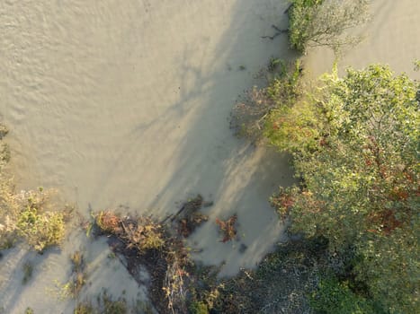 Aerial view of muddy water flowing over the Po riverbanks covering the surrounding land, with a few trees and bushes struggling to survive after heavy fall rainfalls