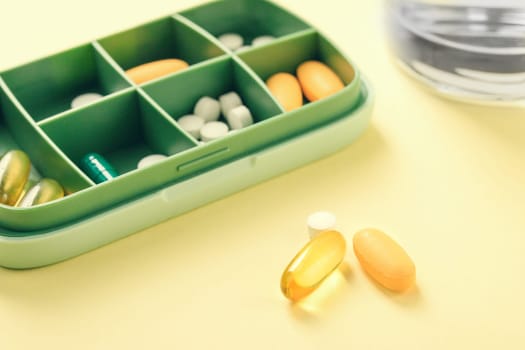 Pill box with various pills and vitamins and microelements omega3 next to water glass.