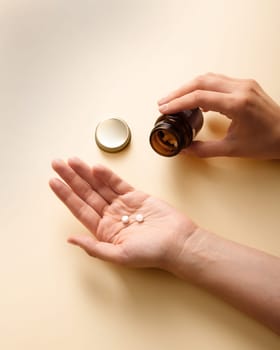 A woman dropped 2 white pills from a bottle into her palm, close-up.