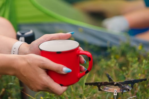 A person cheerfully holding a bright red mug, savoring a warm beverage by a cozy campfire in a tranquil outdoor setting