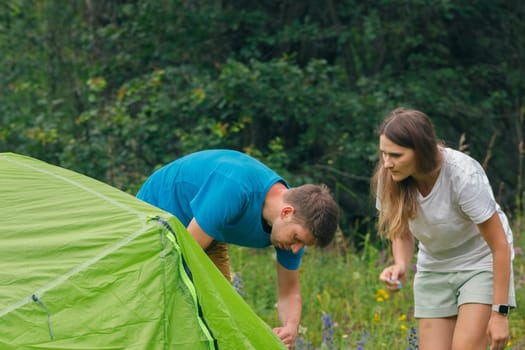 A couple enjoys a delightful camping experience by setting up their vibrant green tent amidst a picturesque landscape