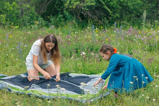 A mother and her daughter are joyfully setting up a tent together in a vibrant, flowerfilled meadow, enjoying nature
