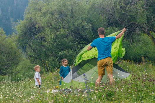 A happy father and his excited kids set up a colorful tent in a lively meadow on a sunny summer day