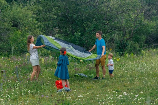 A joyful family is setting up a colorful tent in a lush field, fully embracing outdoor fun together