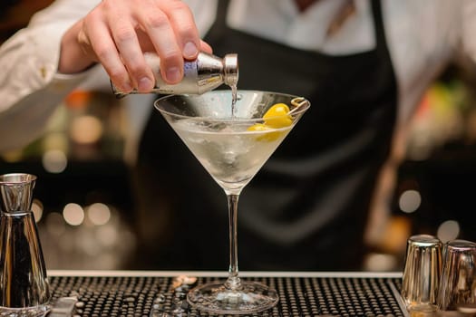 Bartender is pouring a cocktail into a martini glass with olives