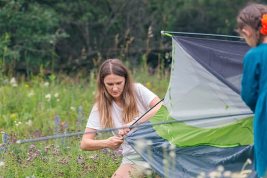 Two very close friends excitedly set up a cozy tent in a beautiful field during their fun camping trip together