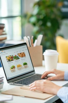 Woman is using a laptop to order food online in a restaurant, browsing the menu and selecting her meal
