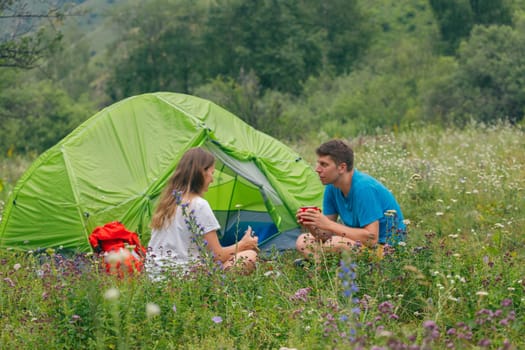 A couple enjoys a peaceful moment, relaxing together by their bright green tent in a gorgeous flowering meadow