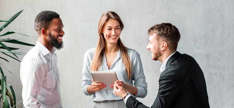 Happy Coworkers Talking Standing Near Desk Having Break At Work In Modern Office. Corporate Lifestyle Concept