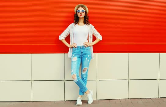Young woman model posing wearing a casual, summer straw round hat on city street over red background