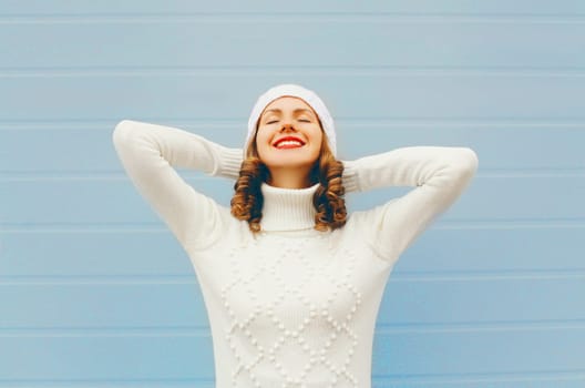 Happy pretty smiling young woman enjoys a good day wearing knitted hat sweater over blue background