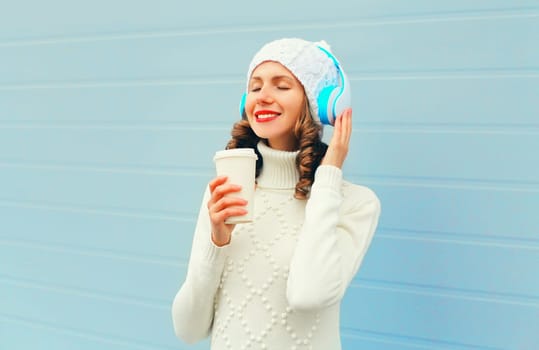 Winter portrait happy woman listens to music in headphones wear hat, sweater on blue background