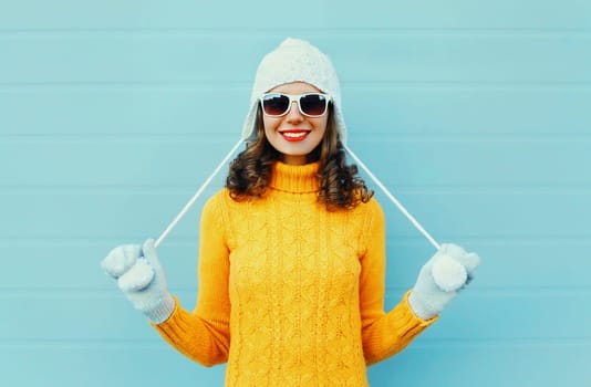 Portrait happy young smiling woman wearing a sunglasses, knitted hat, sweater over blue background