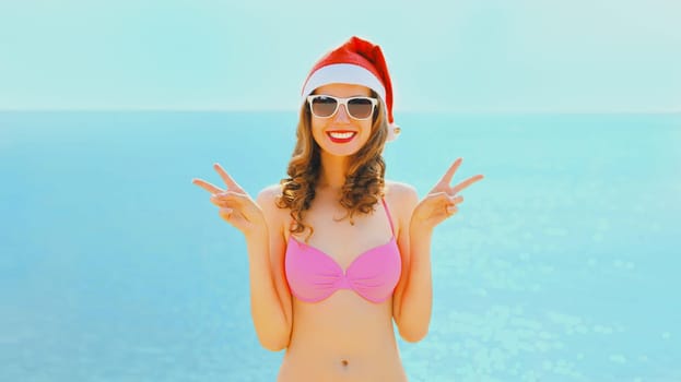 Christmas smiling young woman in red santa hat on beach over sea background