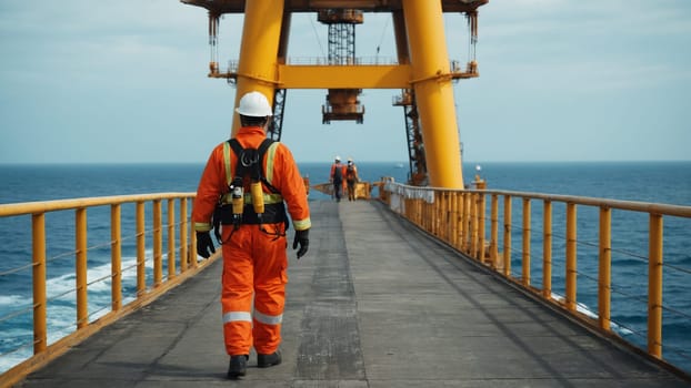 A construction worker in an orange jumpsuit and helmet walks along a wooden platform, with an oil rig and overcast sky visible in the background. The scene illustrates industrial life at sea.