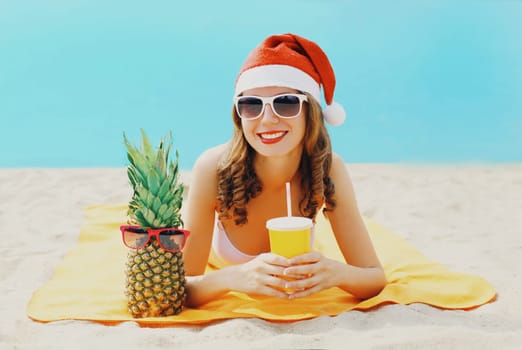 Christmas portrait happy woman in red santa hat with pineapple cup juice lying on beach on sea