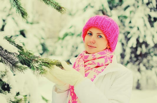 Winter happy smiling woman wear colorful knitted hat scarf near christmas tree over snowy background