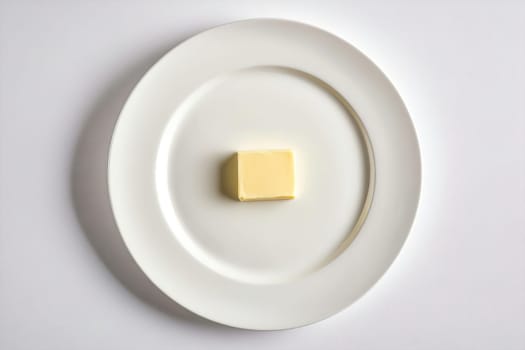A stick of butter sits in the center of a simple white plate, showcasing its smooth texture and creamy yellow hue in a minimalist presentation.