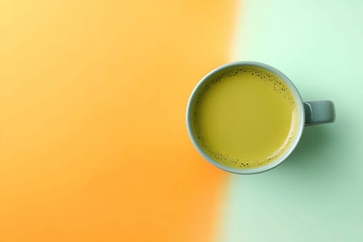 A warm turmeric latte fills a simple mug, resting on a vibrant background that transitions from orange to teal, creating a soothing atmosphere.