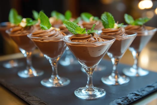 A selection of chocolate mousse desserts arranged in stylish glass cups, each beautifully topped with fresh mint leaves, invites sweet indulgence.