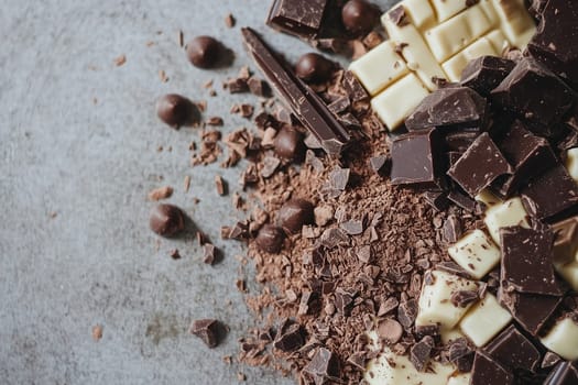Various types of chocolate, including dark, milk, and white varieties, are artfully arranged on a textured surface, with some pieces broken and shavings scattered about.