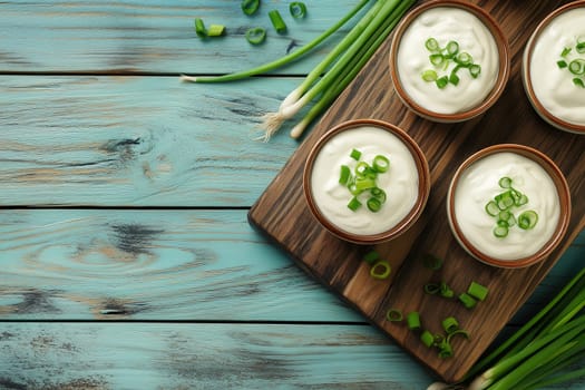 Three bowls of creamy dip sit on a wooden platter, topped with freshly chopped green onions. The vibrant teal background enhances the rustic vibe and appetizing presentation.