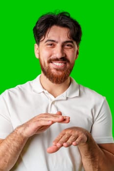 A young man in a white polo shirt dances energetically against a vibrant green background close up
