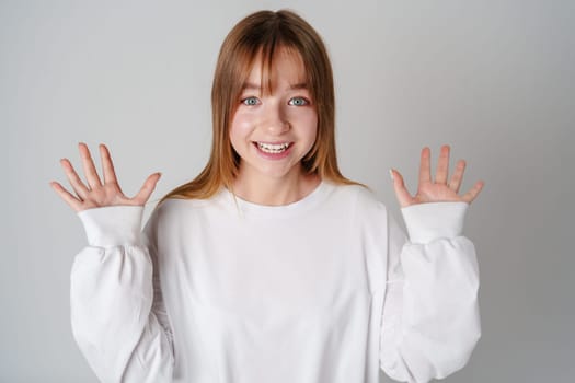 A surprised child wearing a white long-sleeve shirt and blue jeans expresses confusion in a studio setting close up