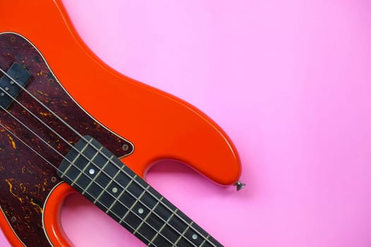 Red electric bass guitar on a pink background. Close-up image.