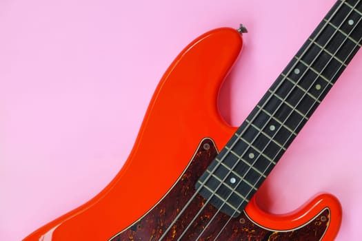 Red electric bass guitar on a pink background. Close-up image.